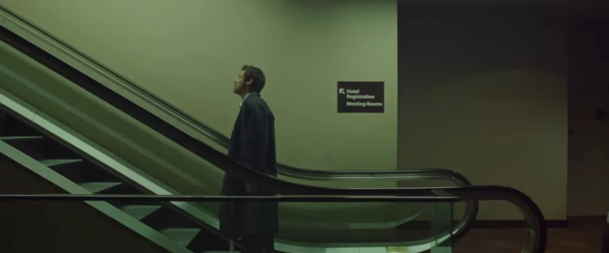 Frame do clipe “Aperture”, de Harry Styles: cantor em pé em uma escada rolante, em cenário urbano com luz fria e atmosfera cinematográfica.