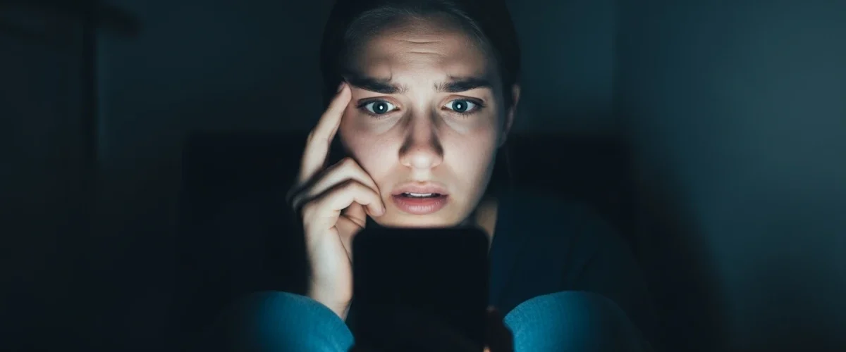 Mulher assustada olhando para o celular, representando a cultura do cancelamento e a autocensura nas redes sociais