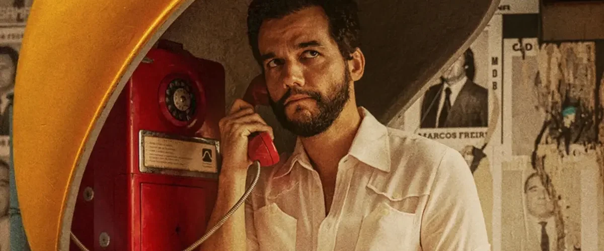 Wagner Moura em cena do filme O Agente Secreto usando um orelhão durante a ditadura militar no Brasil