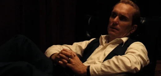 Robert Duvall como Tom Hagen em O Poderoso Chefão sentado em poltrona em cena do filme