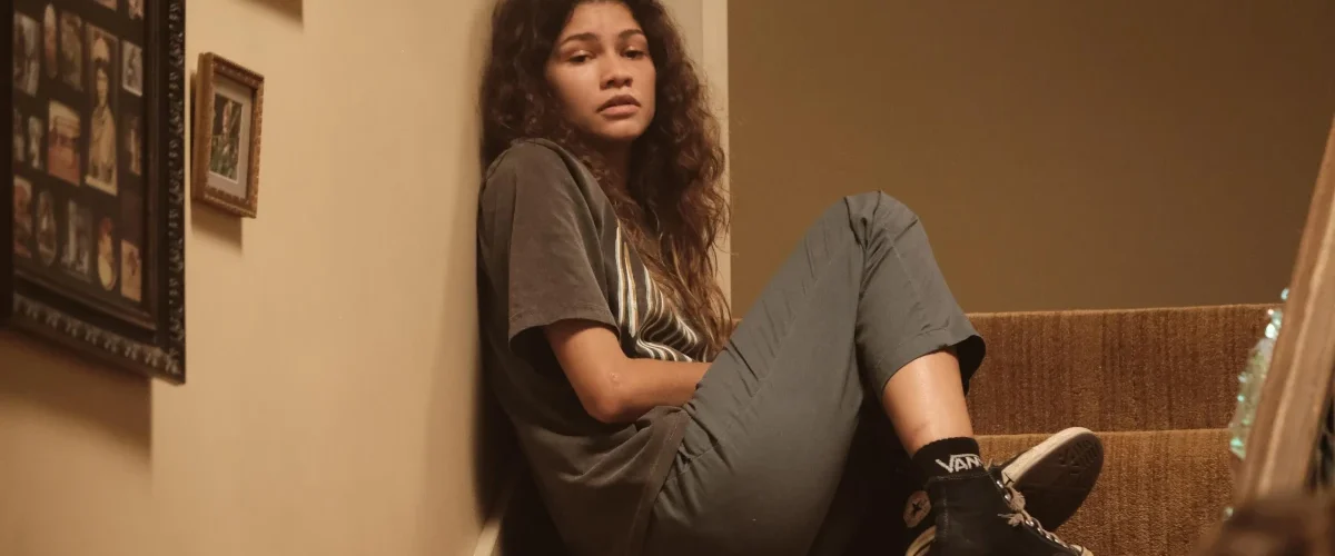 Rue Bennett sentada na escada em Euphoria, expressão introspectiva, estética dramática da série