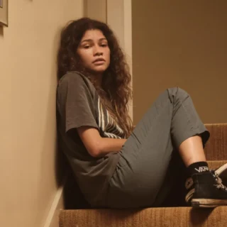 Rue Bennett sentada na escada em Euphoria, expressão introspectiva, estética dramática da série