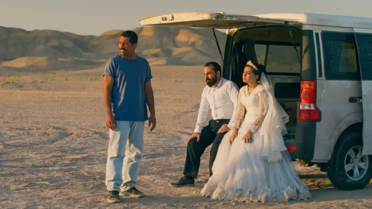 Casal de noivos e homem ao lado de uma van no deserto em cena do filme Foi Apenas um Acidente de Jafar Panahi