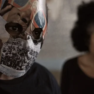 Jovem com máscara feita de recortes históricos em cena do documentário Hora do Recreio de Lúcia Murat