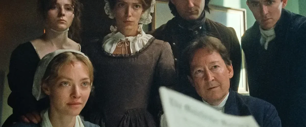 Grupo de personagens em ambiente do século XVIII observando documento em cena do filme O Testamento de Ann Lee
