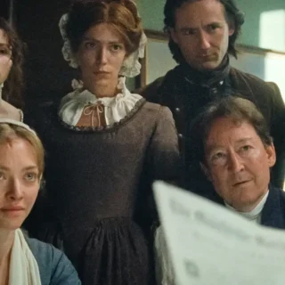 Grupo de personagens em ambiente do século XVIII observando documento em cena do filme O Testamento de Ann Lee