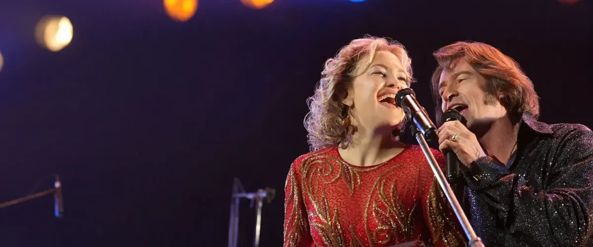 Hugh Jackman e Kate Hudson cantando no palco no filme Song Sung Blue Um Sonho a Dois