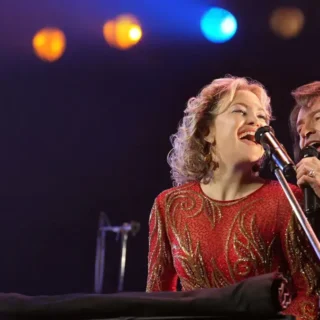 Hugh Jackman e Kate Hudson cantando no palco no filme Song Sung Blue Um Sonho a Dois