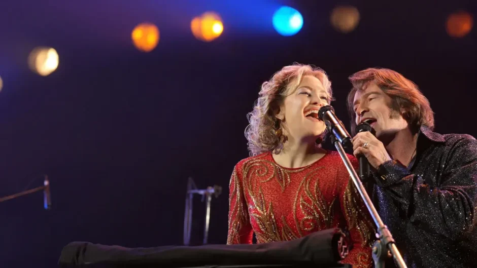 Hugh Jackman e Kate Hudson cantando no palco no filme Song Sung Blue Um Sonho a Dois