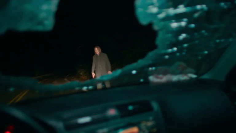 Entidade sombria parada no meio da estrada durante a noite em Passageiro do Mal (2026)