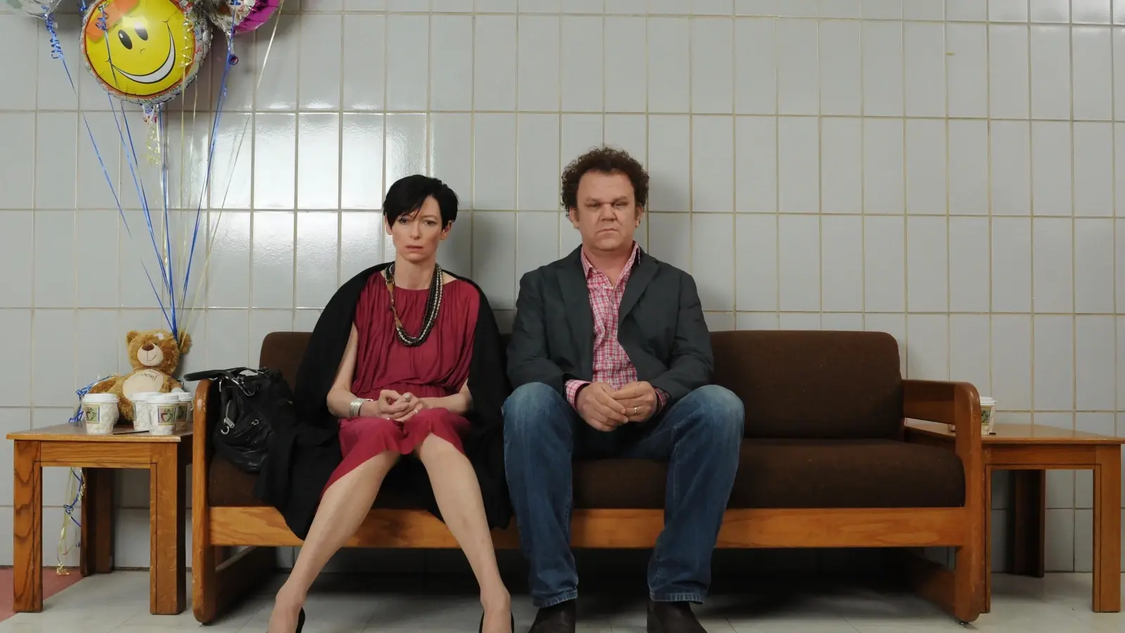 Cena do filme Precisamos Falar Sobre o Kevin com Tilda Swinton e John C. Reilly sentados em uma sala de hospital